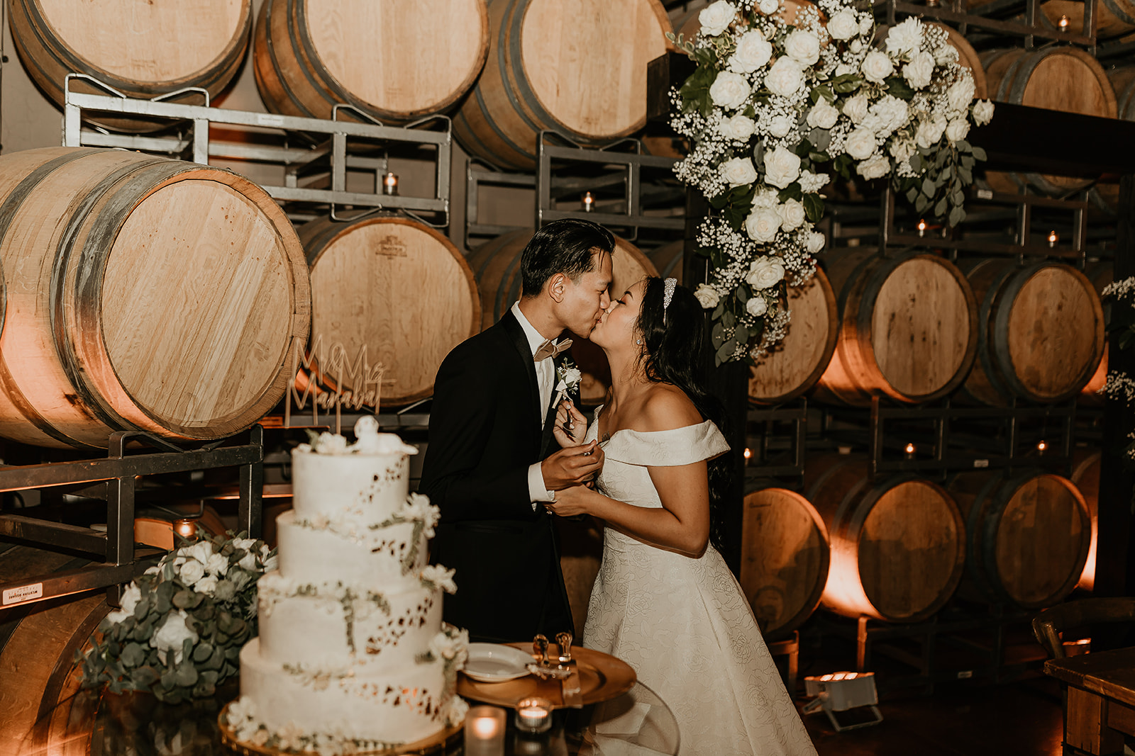 A couple celebrationg their wedding at Domenico Winery San Carlos shotin front of the cask wall during cake cutting