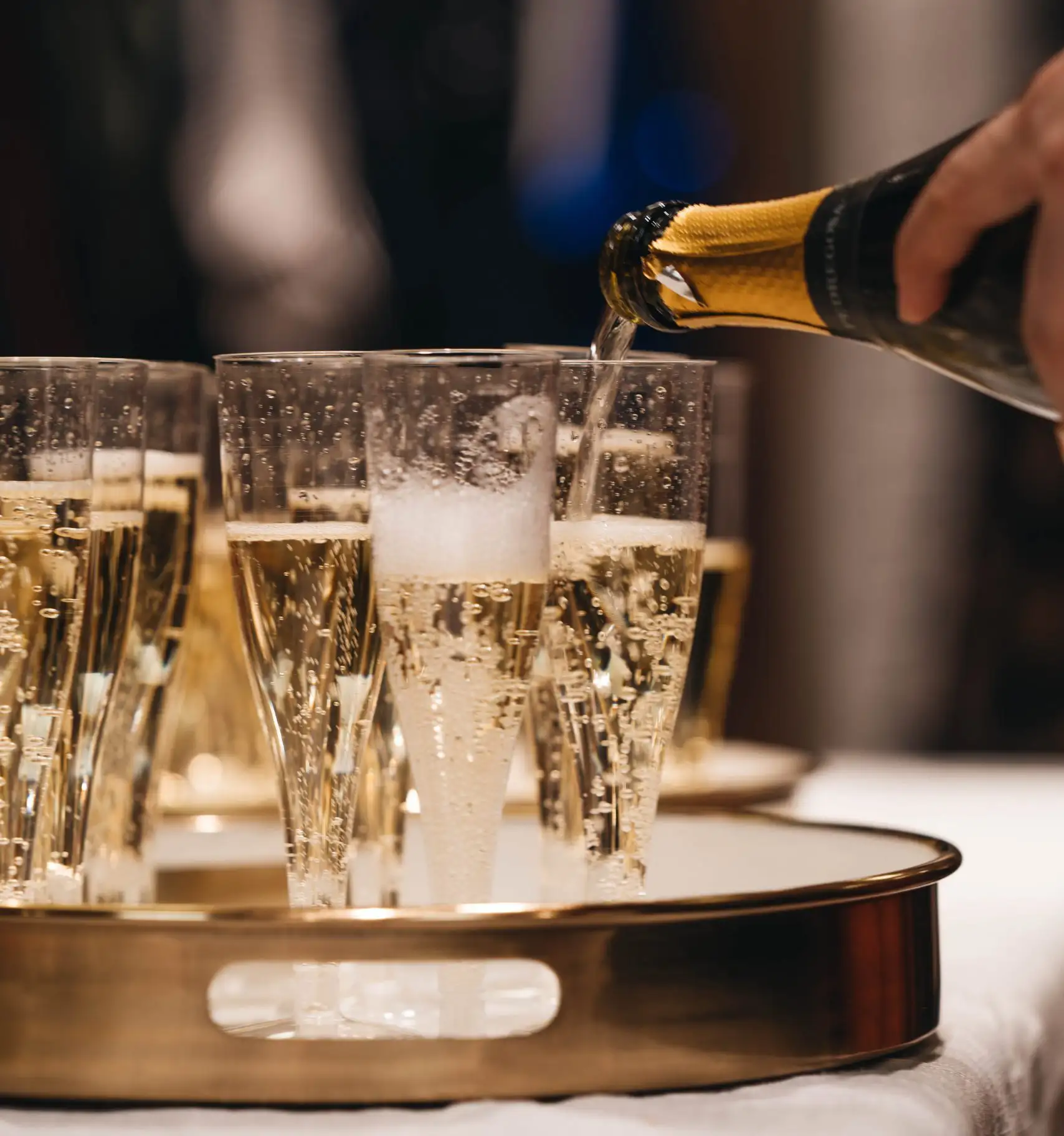 Champagne being poured into flutes on a serving tray during a holiday celebration.