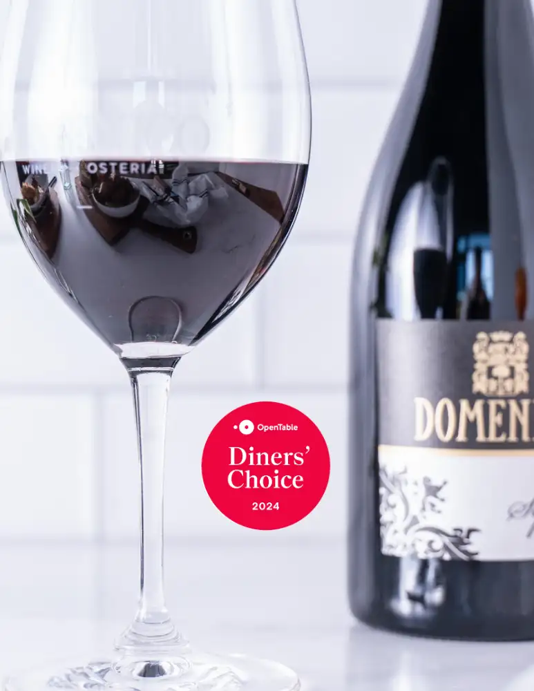 Domenico Winery & Osteria Receives OpenTable Diners' Choice Award | Domenico Winery Close-up of a red wine glass with a bottle of Domenico wine in the background, featuring the OpenTable Diners' Choice 2024 badge.