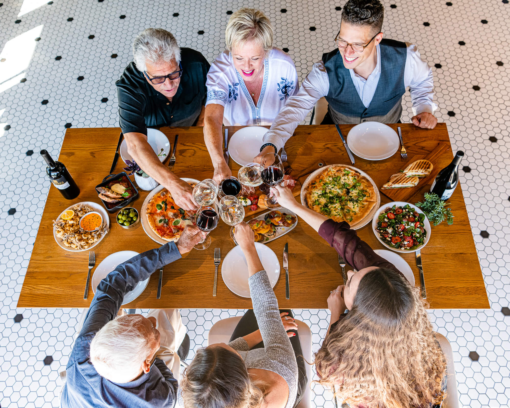 A family of 6 people enjoying dinner at the Osteria at Domenico with glasses of wine and pizza