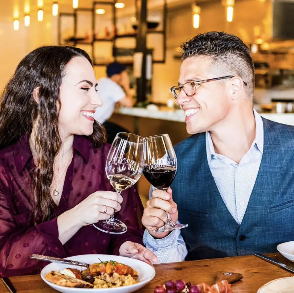 Italian Food 101: Pairing Wine with Pasta | Domenico Winery Marina and Dominick toasting with wine glasses at a restaurant, smiling at each other.