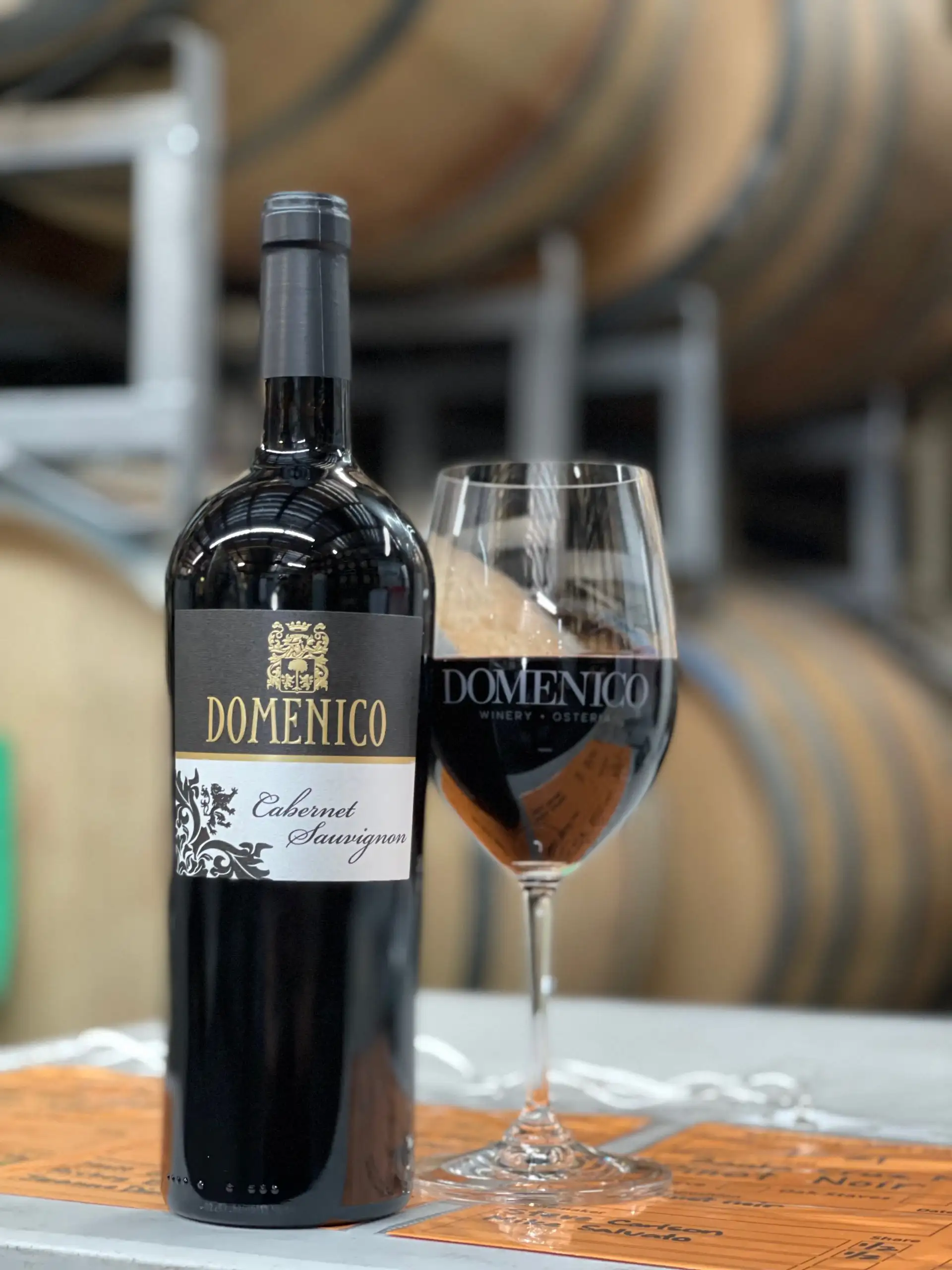Domenico Winery Wins Gold at SFIWC | Domenico Winery Bottle of Domenico Cabernet Sauvignon red wine next to a filled wine glass in a winery cellar