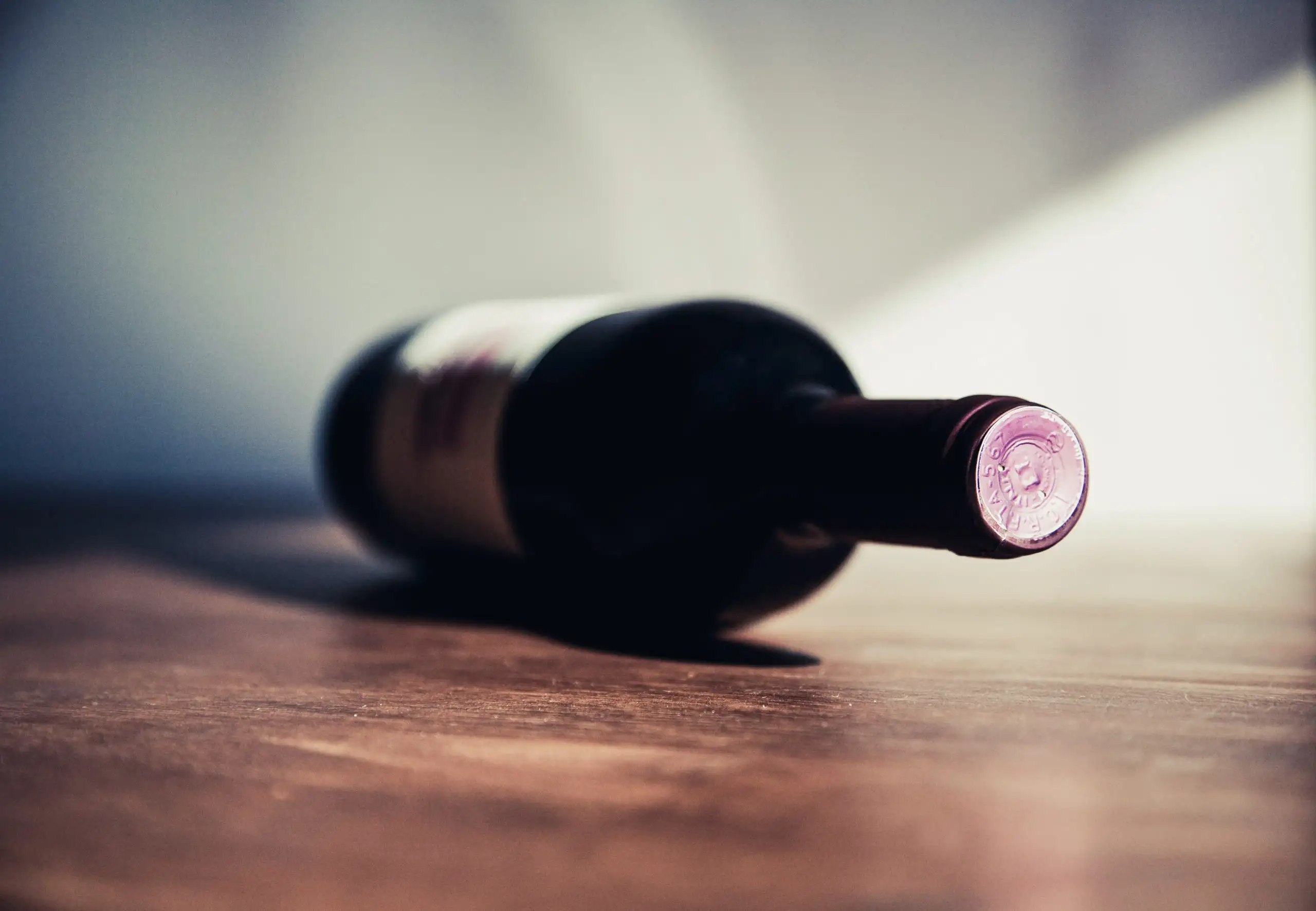 Close-up of a wine bottle lying on a wooden surface with a purple seal on the cap.