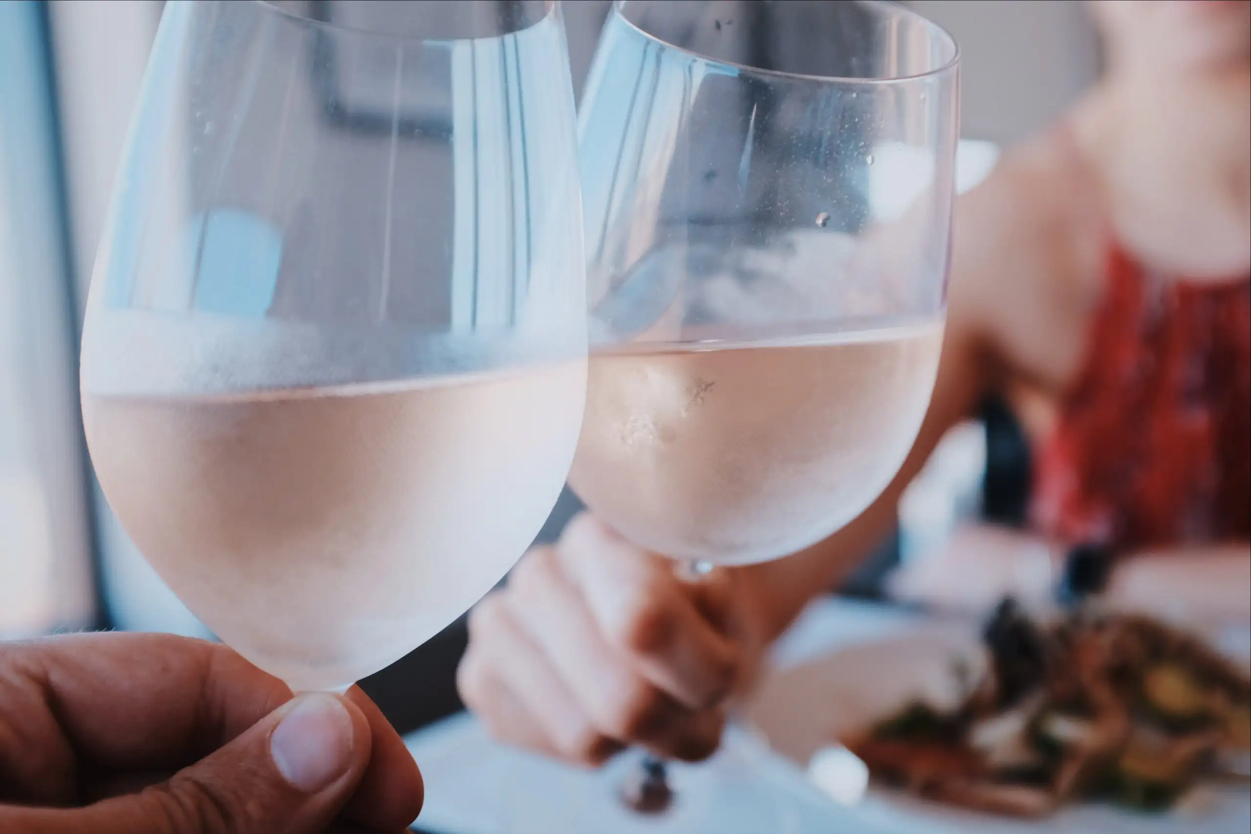Two people clinking glasses of rosé wine during a meal, with a soft, light-filled background.