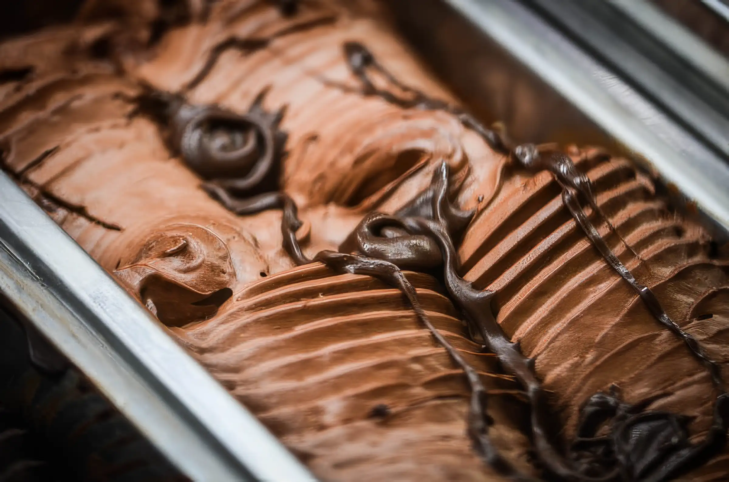 Close-up of creamy chocolate gelato with chocolate drizzle in a metal container
