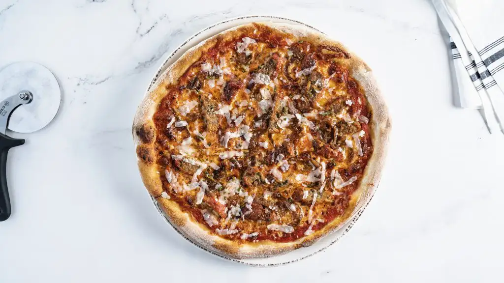How to Pair Wine with Pizza (Guide) | Domenico Winery Classic pizza topped with seasoned beef, onions, and melted cheese, placed on a marble countertop with a pizza cutter.