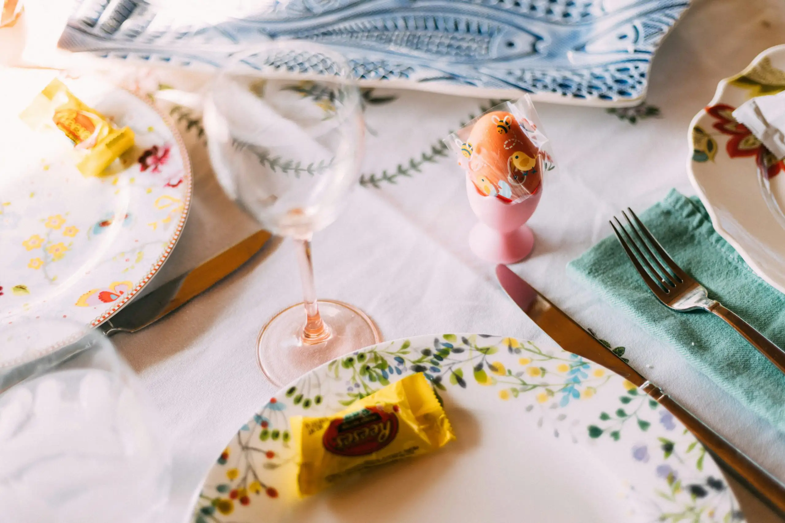 Hand reaching toward a bowl of decorated Easter eggs surrounded by greenery and small purple flowers.
