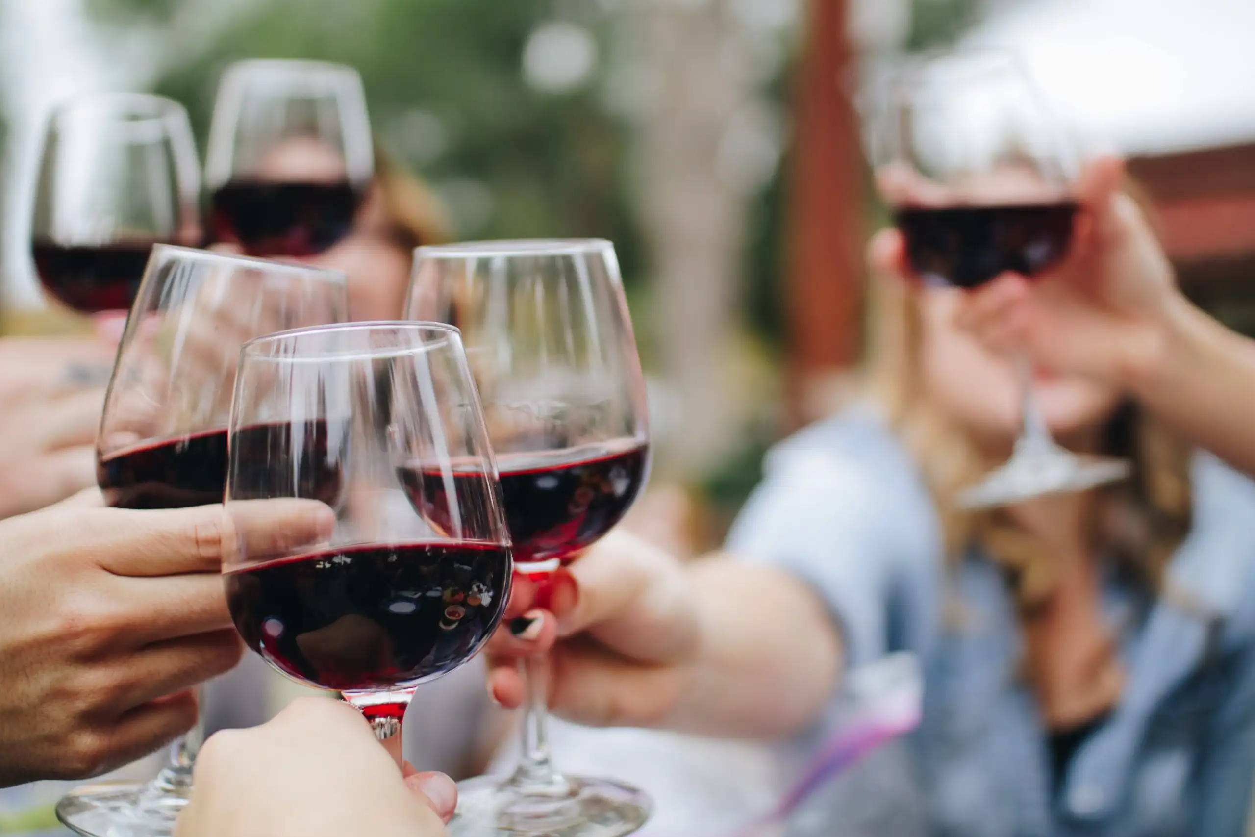 Italian Grapes 101: Sangiovese | Domenico Winery A group of friends holding up glasses of red wine for a toast in a blurred outdoor setting.