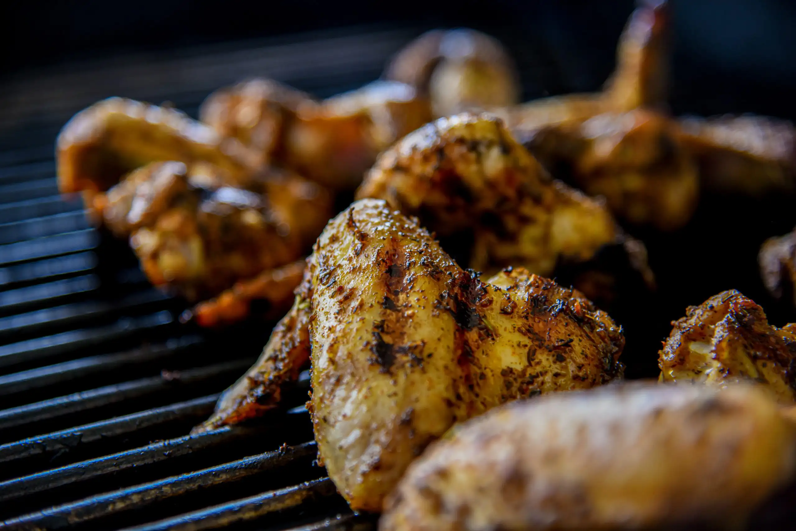 The Ultimate Super Bowl Wine Pairings | Domenico Winery Close-up of seasoned chicken wings grilling on a black metal barbecue grate with charred grill marks.