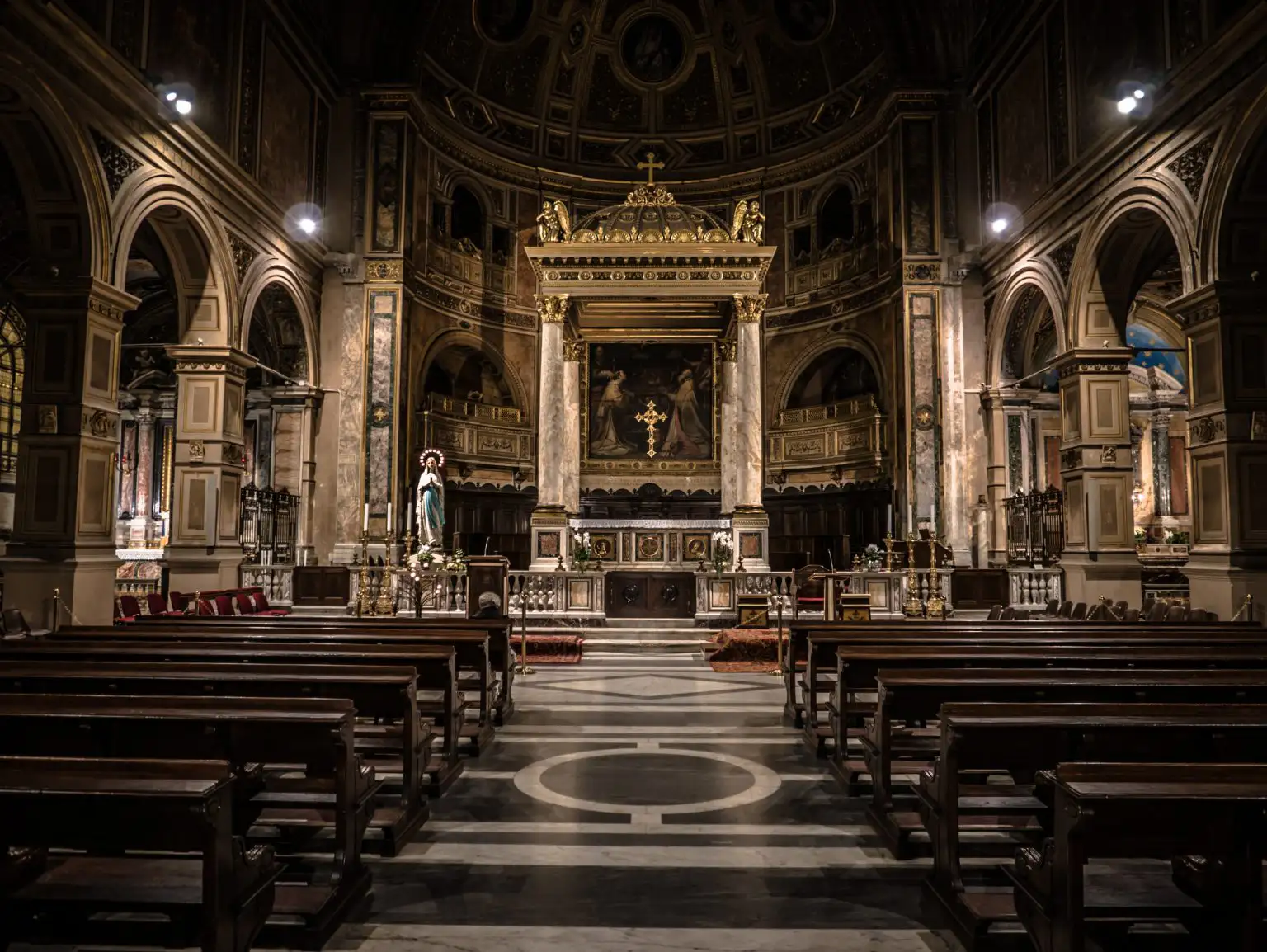 Italian Christmas Traditions Everyone Should Know | Domenico Winery The interior of a grand cathedral showing rows of dark wooden pews leading toward a gold-ornamented altar under a high domed ceiling.