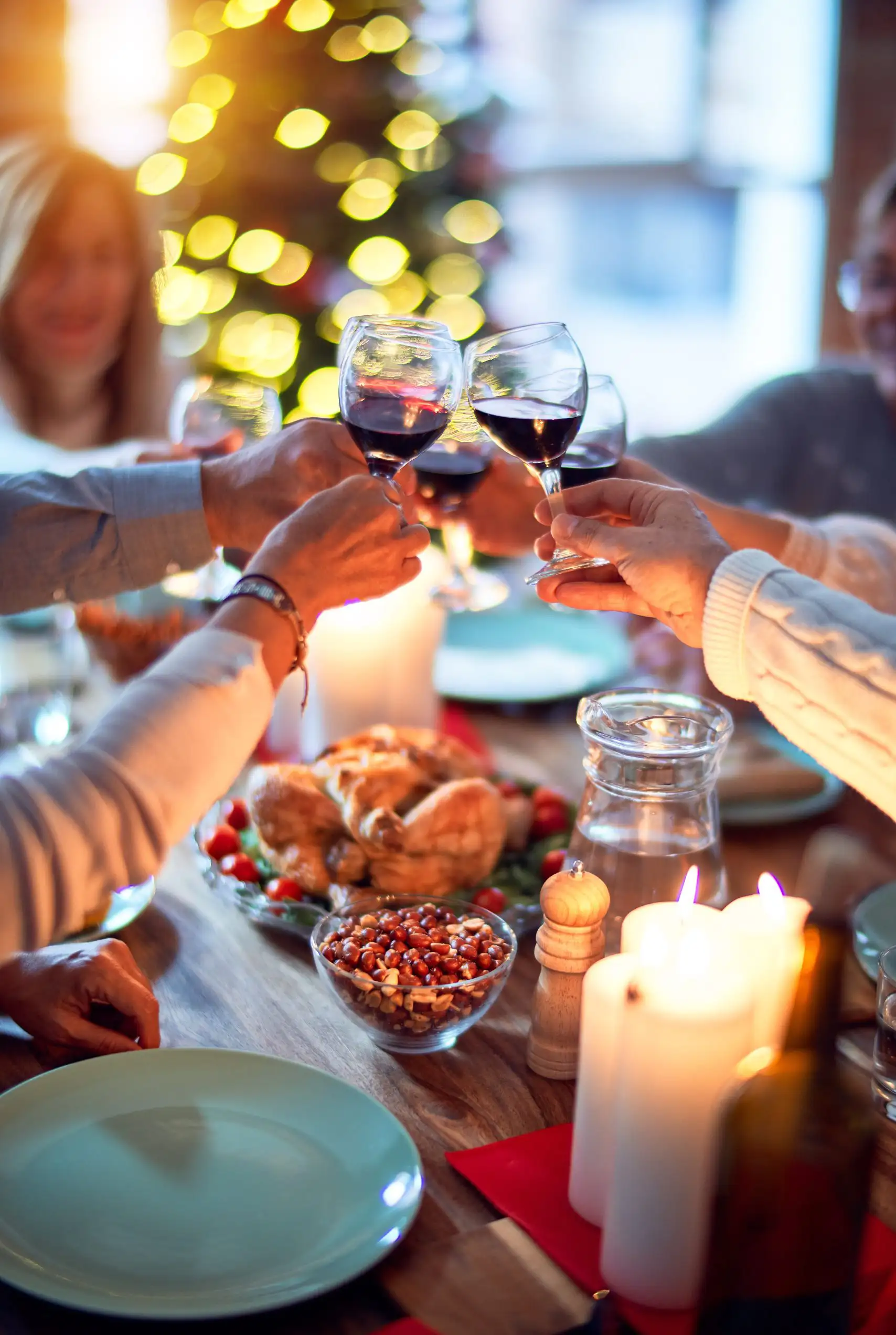 People clinking wine glasses in celebration around a festive holiday dinner table.