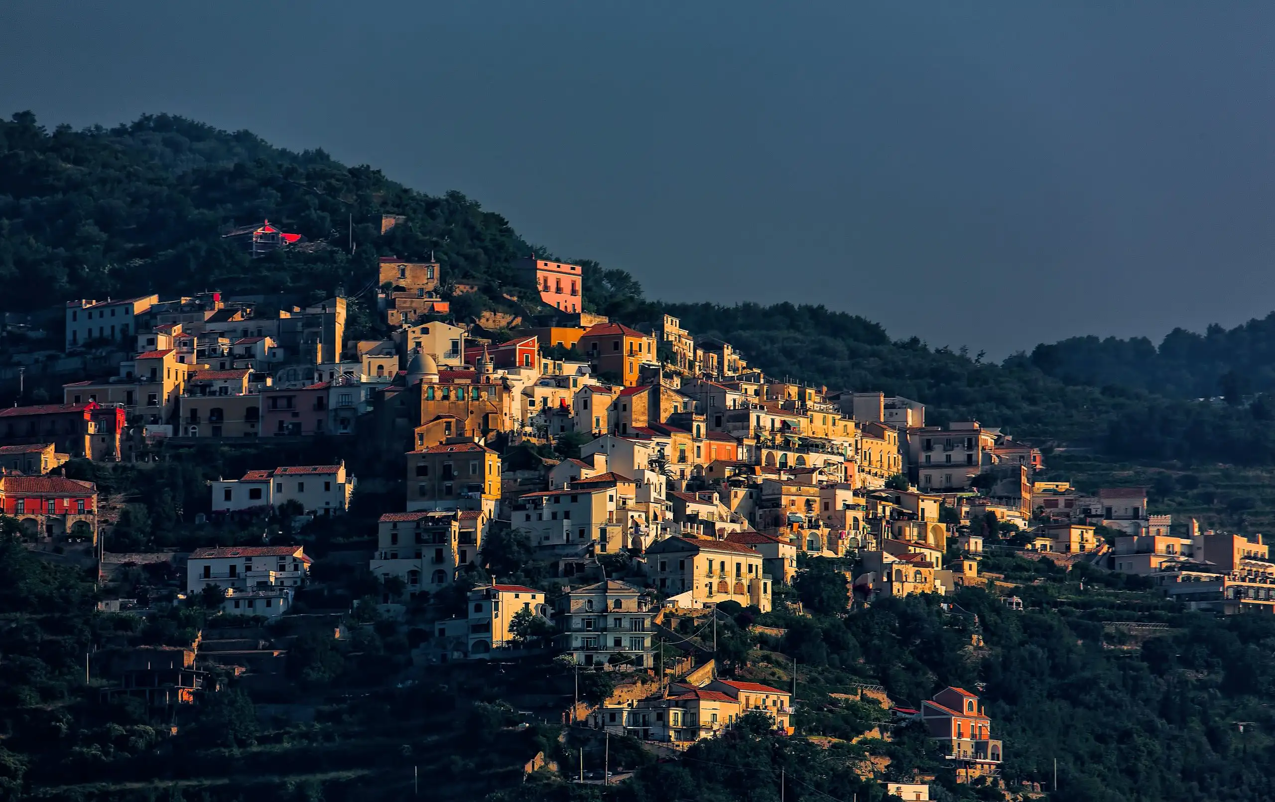 Colorful houses clustered on a hillside in a traditional Italian mountain village during golden hour.