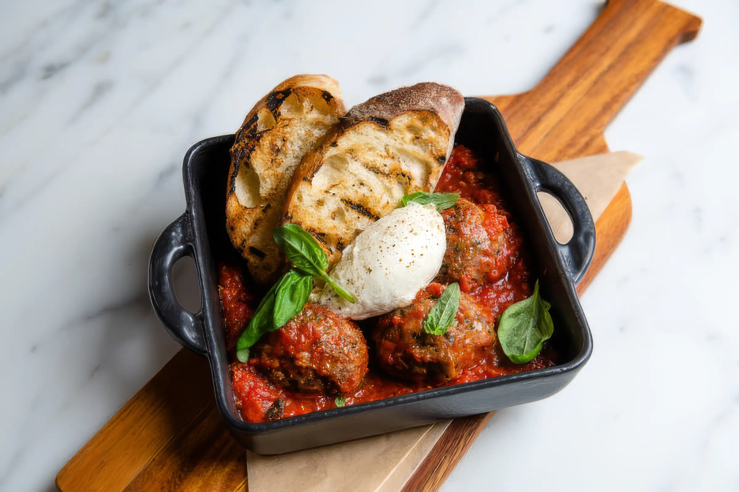 Italian meatballs served in marinara sauce topped with burrata cheese and basil with grilled bread