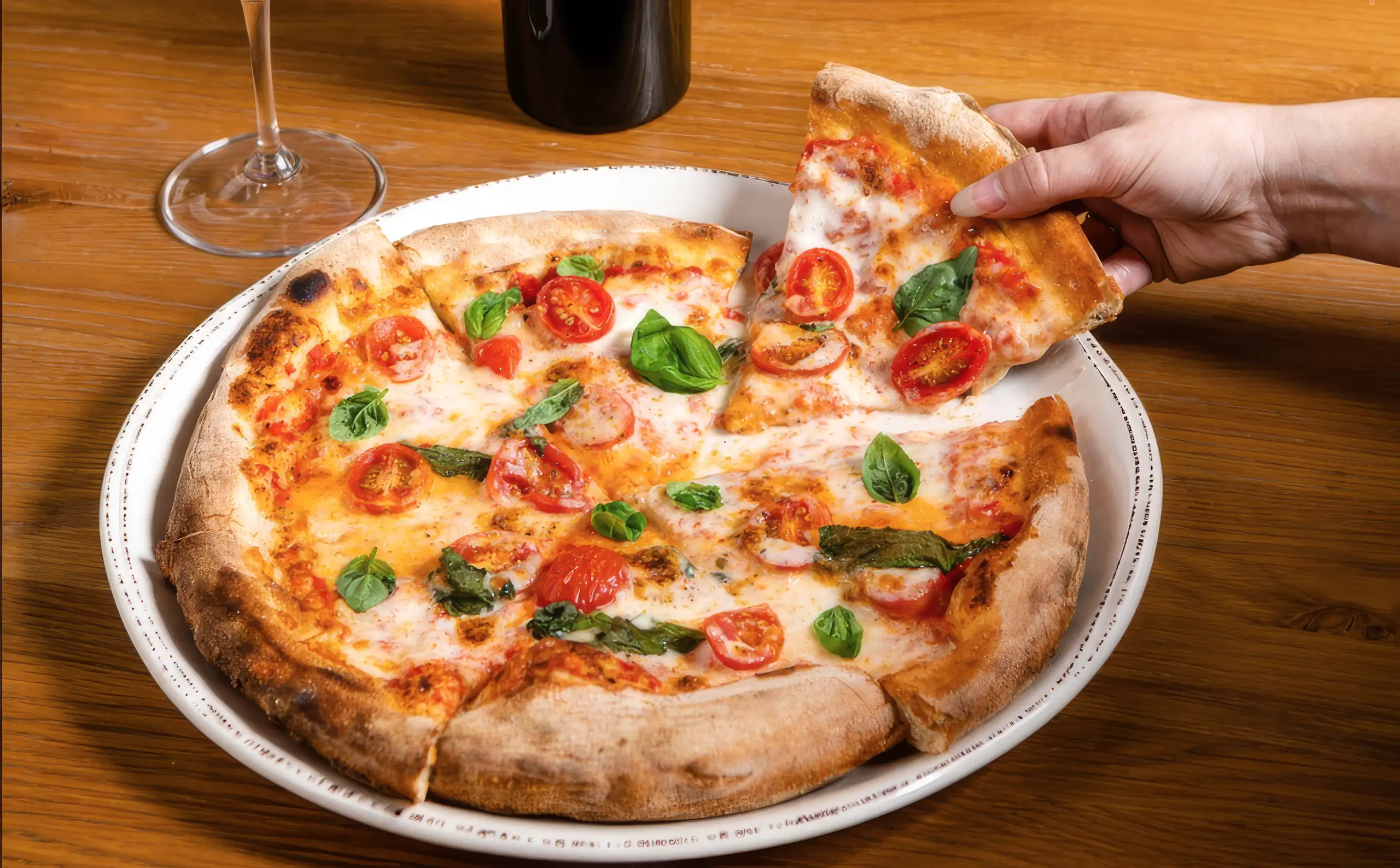 Margherita pizza with mozzarella, cherry tomatoes and basil with a slice being lifted