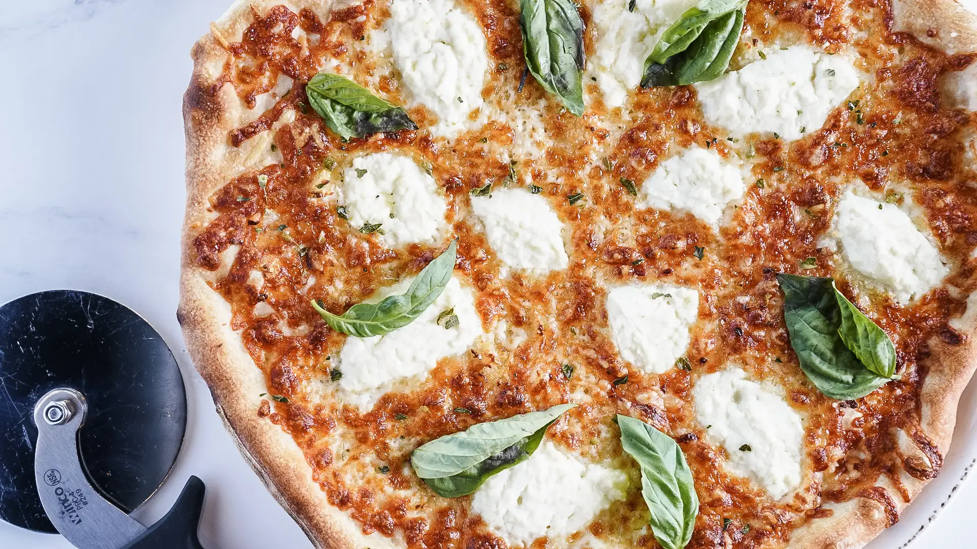 Italian Food 101: Pairing Wine with Pizza | Domenico Winery A delicious margherita pizza topped with fresh basil leaves and dollops of ricotta cheese, showcasing a golden, crispy crust.
