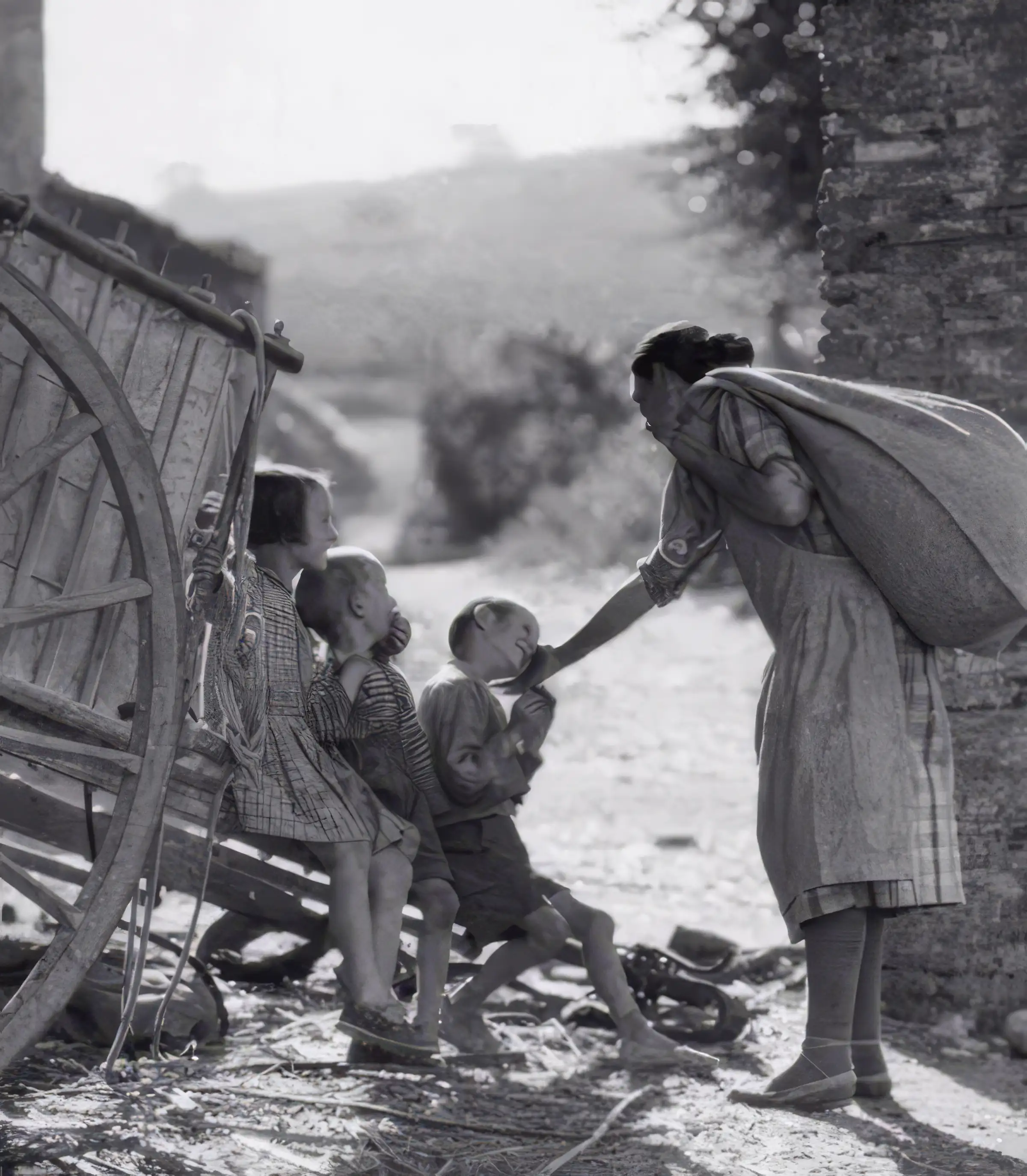 Woman speaking to three young children sitting beside a wooden cart on a rural dirt road, vintage black-and-white photograph.