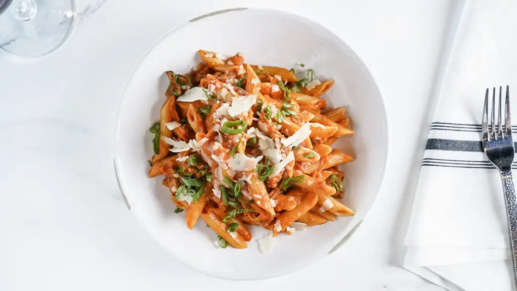 Italian Food 101: Pairing Wine with Pasta | Domenico Winery Plate of penne pasta with tomato sauce, grated parmesan cheese, and chopped green onions on a white table