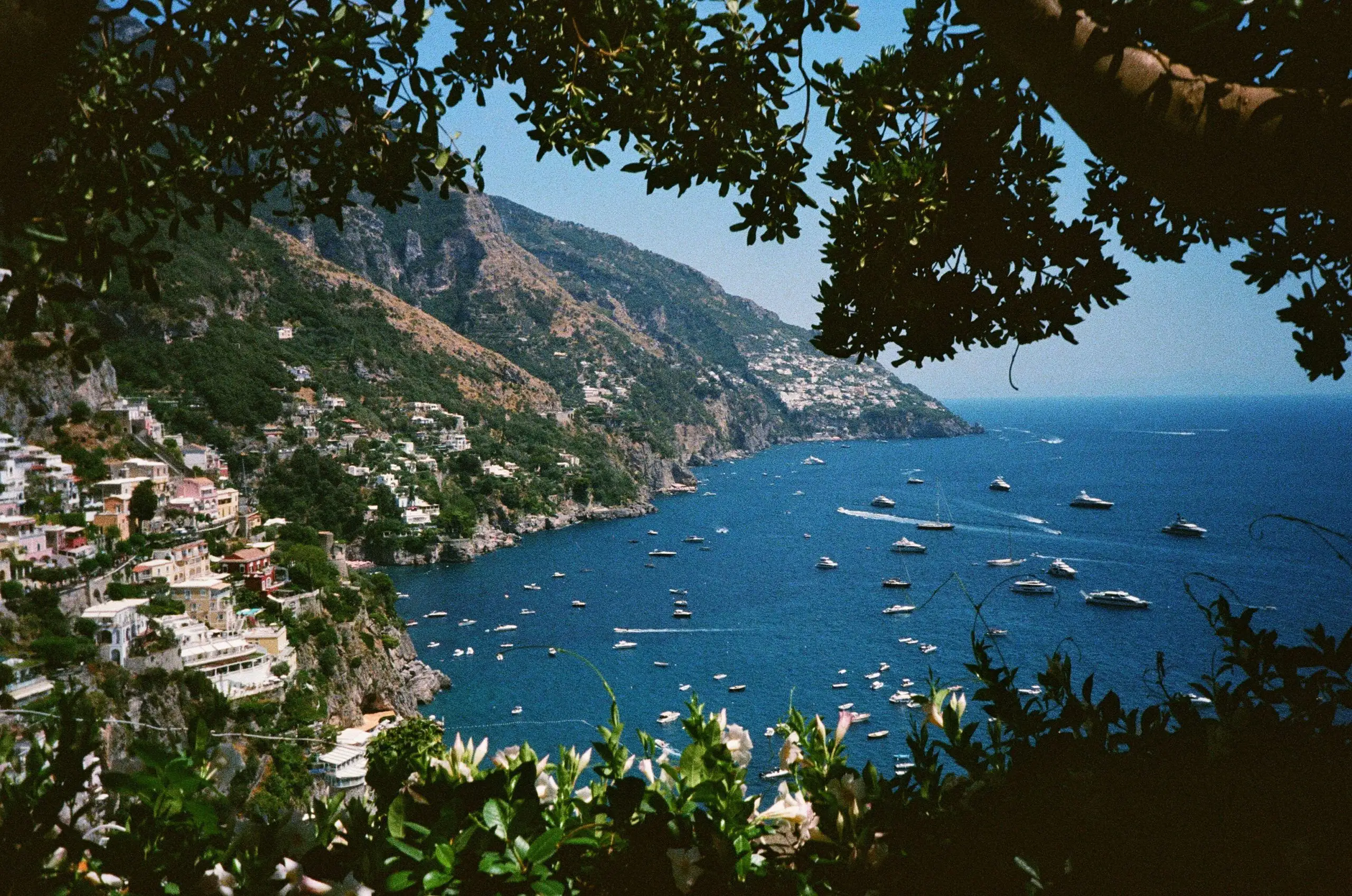 Panoramic view of Positano on the Amalfi Coast in Italy, with boats floating in the blue sea, framed by lush greenery.