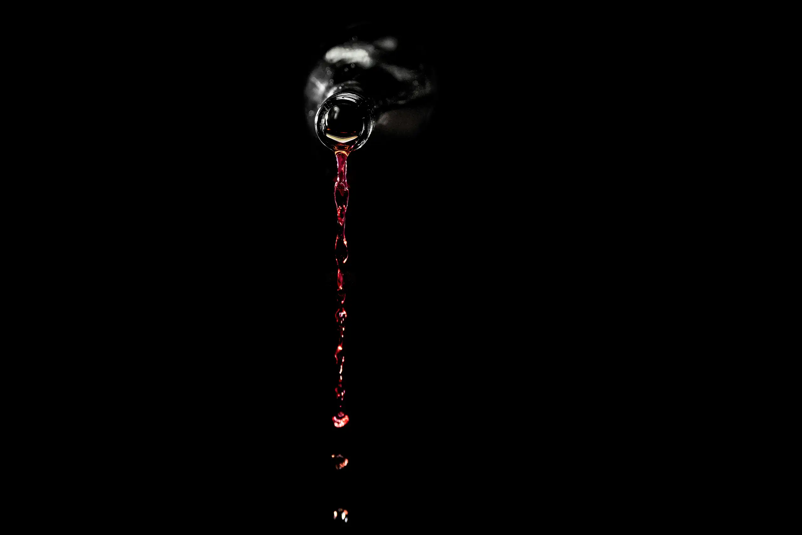 Red wine being poured from a bottle against a dark background with a visible stream of liquid