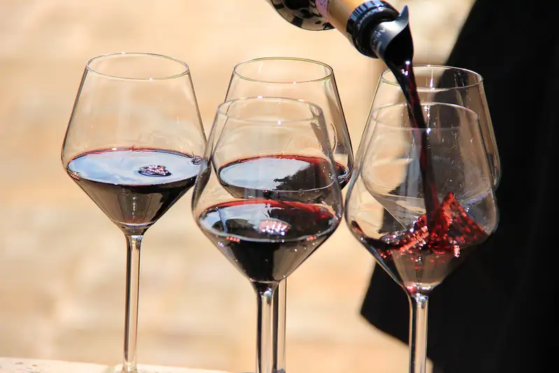 Pouring red wine from a bottle into wine glasses, with wine splashing in the glass.