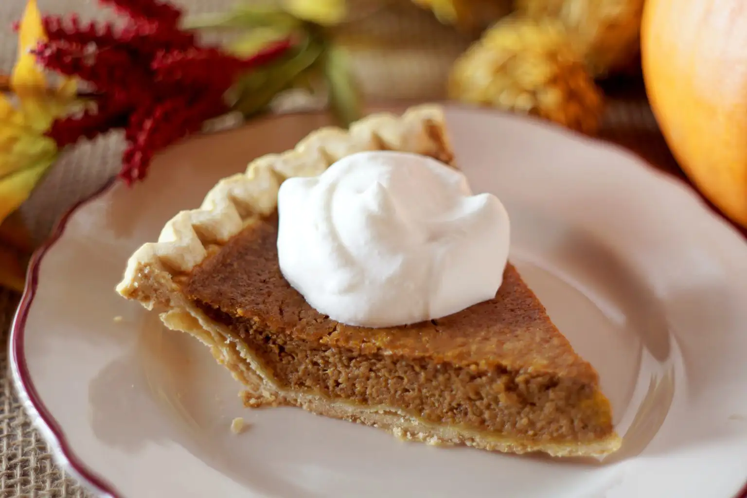 Wine and Pie Pairings that Will Change Your Life | Domenico Winery A slice of pumpkin pie topped with a dollop of whipped cream on a decorative plate.