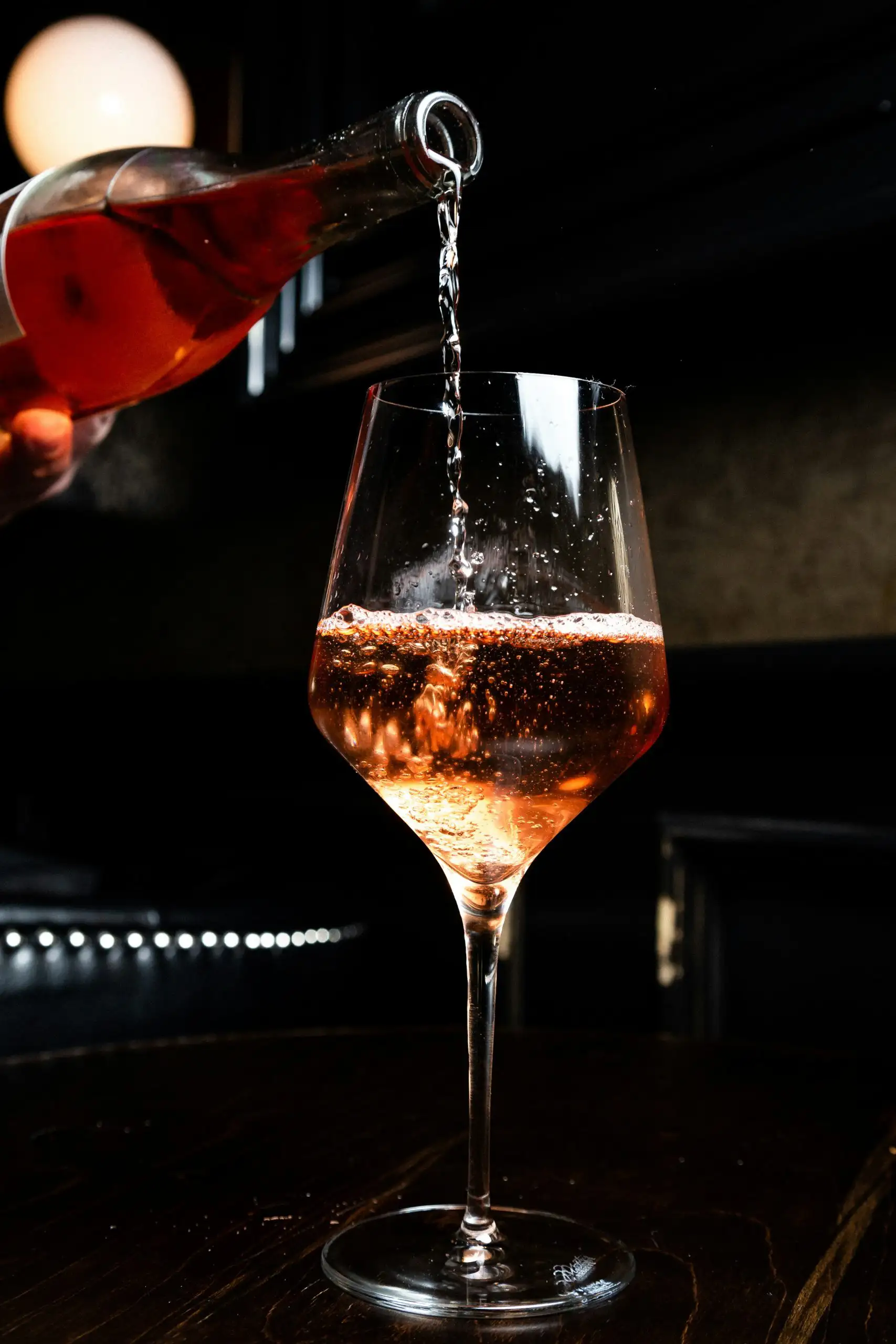 Rosé wine being poured from a bottle into a clear wine glass with bubbles visible.