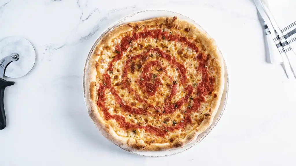 How to Pair Wine with Pizza (Guide) | Domenico Winery Simple cheese pizza with tomato sauce and a golden crust, placed on a marble countertop with a pizza cutter.