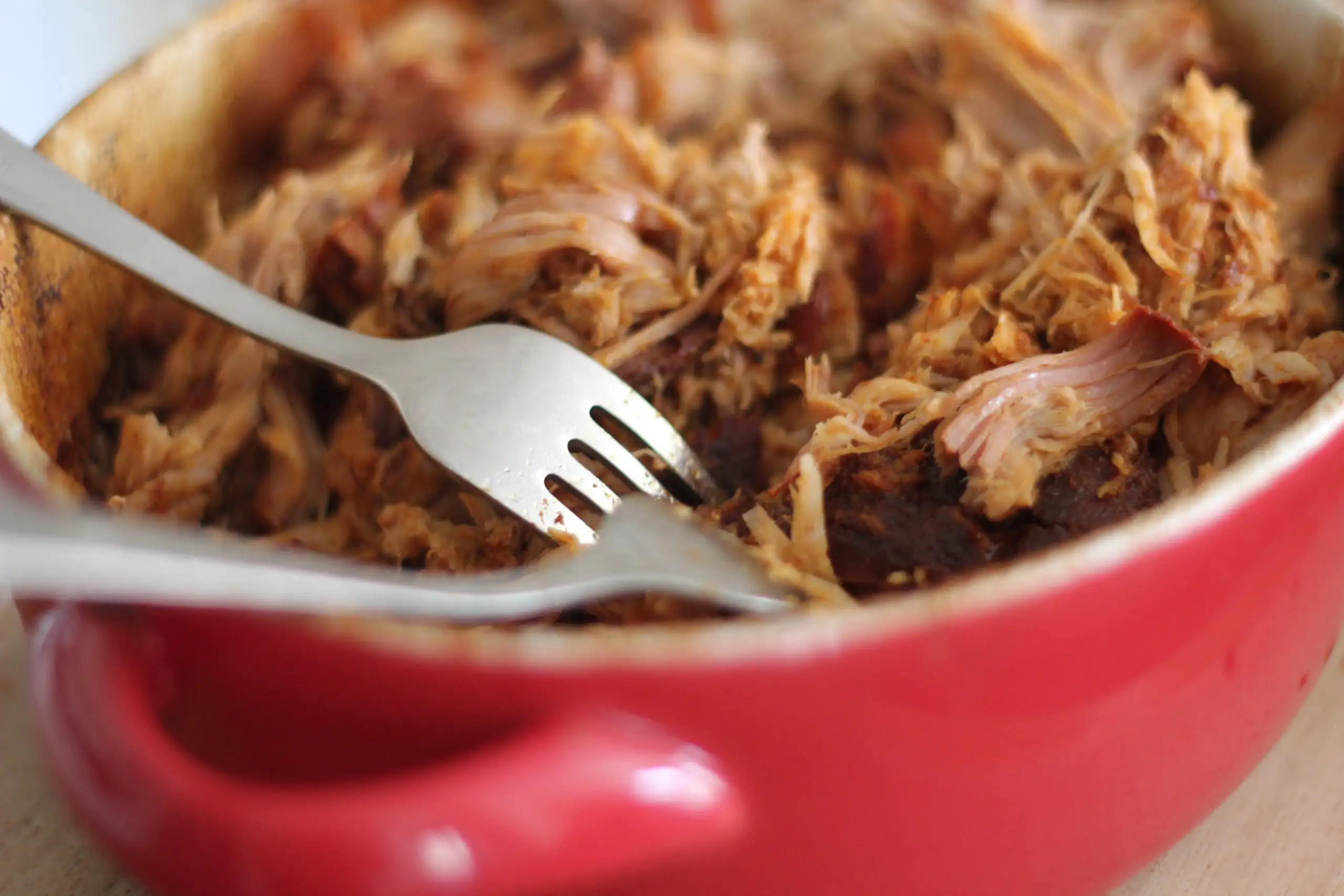 The Ultimate Super Bowl Wine Pairings | Domenico Winery Tender shredded pulled pork in a red ceramic Dutch oven with two silver forks used for shredding.