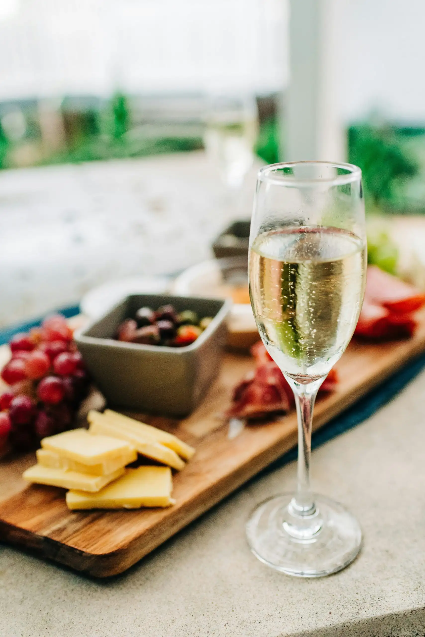 A glass of sparkling wine next to a cheese platter with grapes, cheese, and cured meats.