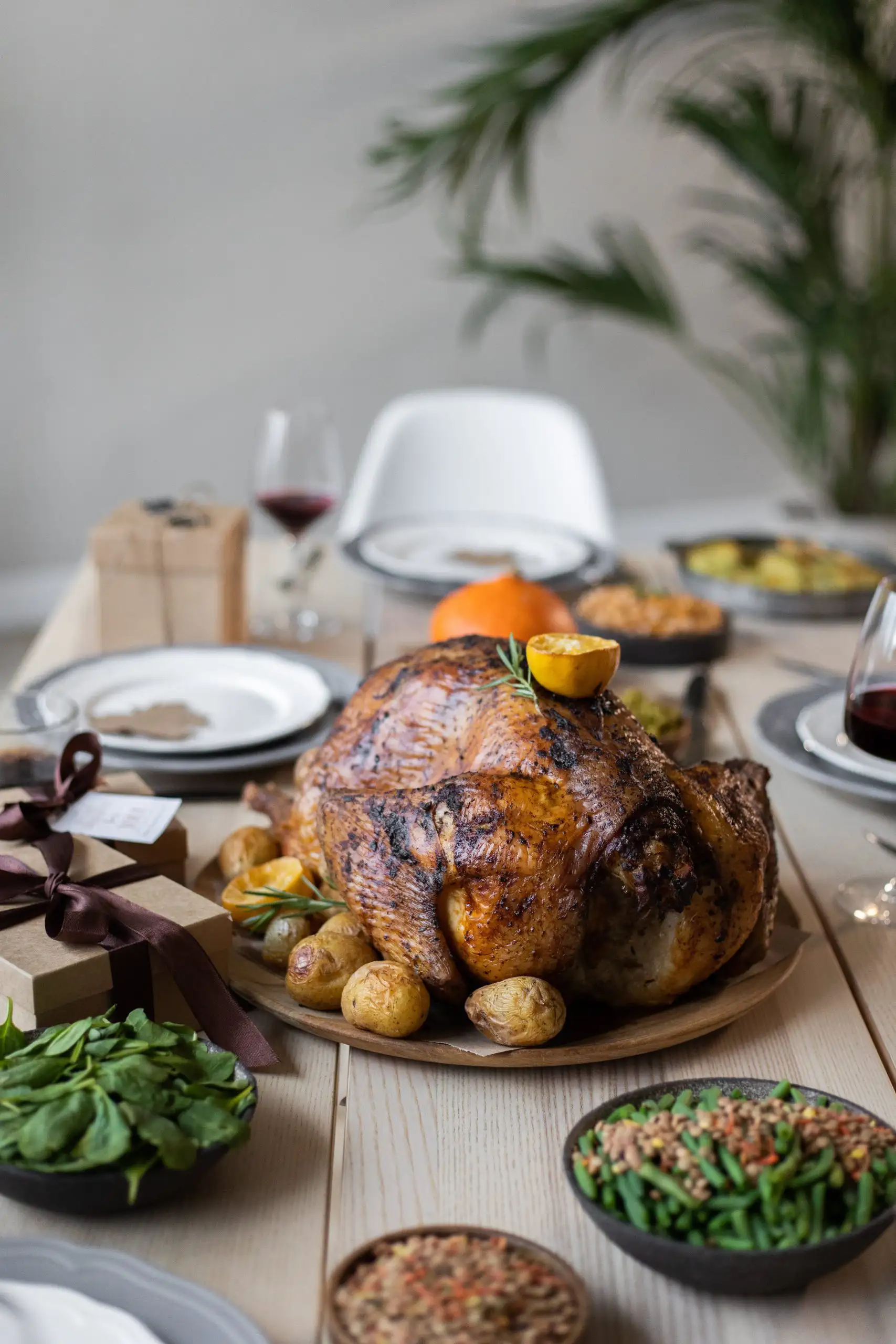 A beautifully roasted chicken with potatoes and vegetables on a table set for Thanksgiving dinner.