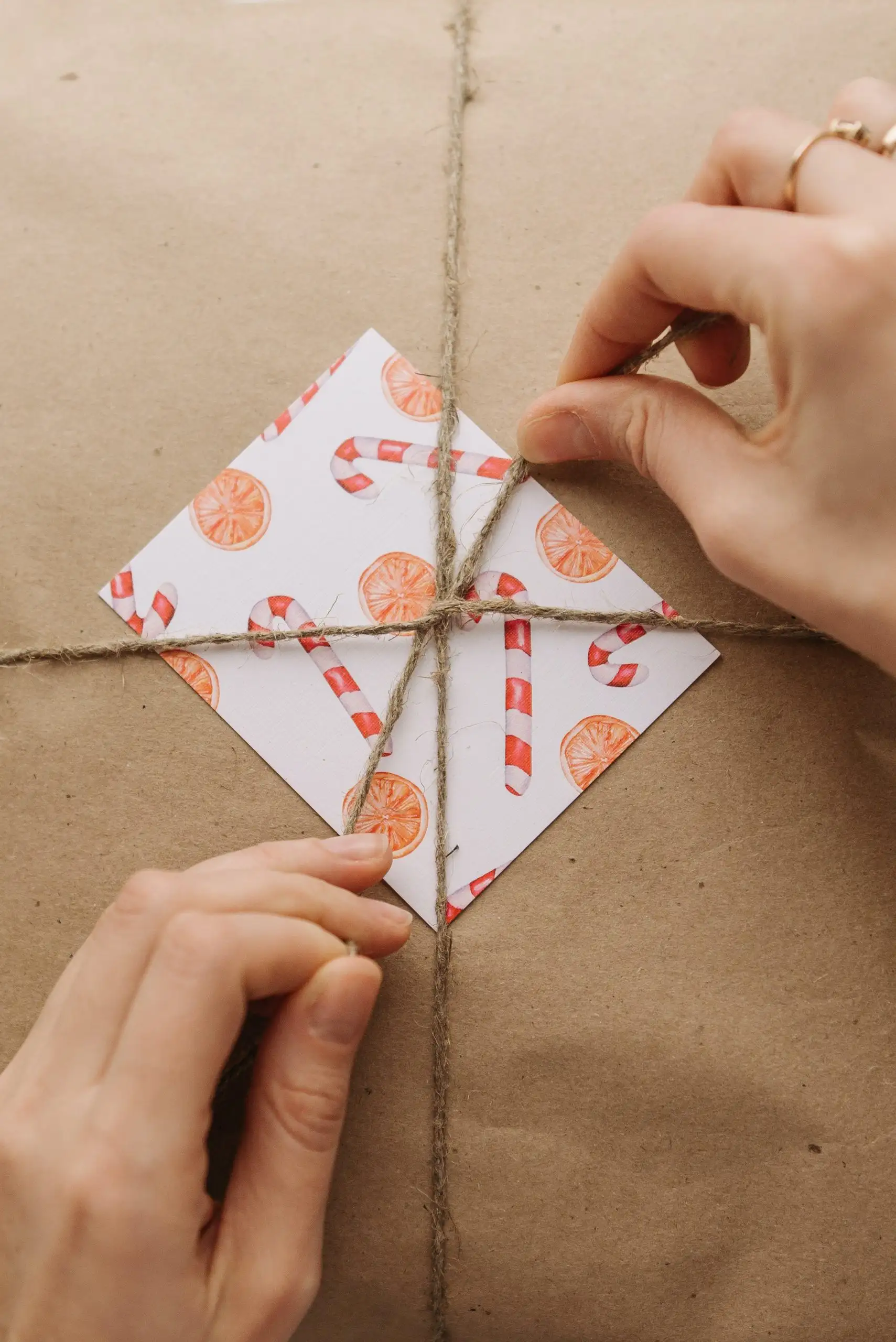 Hands tying twine around a wrapped gift with a festive candy cane patterned card